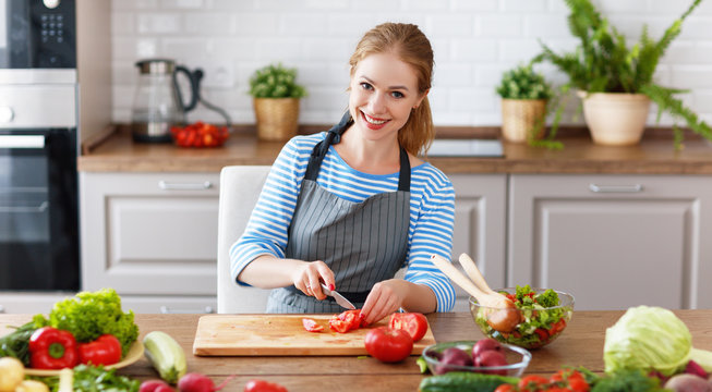happy woman preparing vegetable salad in kitchen