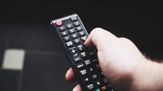 Close up of TV remote changing channels. Channel surfing, focused on the hand and remote control.