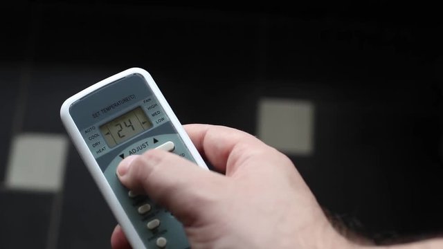 Changing room temperature with air conditioner remote controller. Air conditioner and remote control in hot summer weather