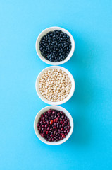 Tree types of dried beans in a white bowls on a light blue background. Top view. Healthy eating concept.