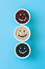 Tree types of dried beans in a white bowls on a light blue background. Smile inscription. Top view. Healthy eating concept.