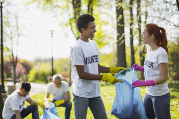 Environmental volunteering. Positive two volunteers holding garbage bag and looking at each other