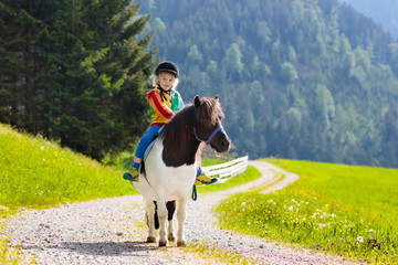 Kids riding pony. Child on horse in Alps mountains