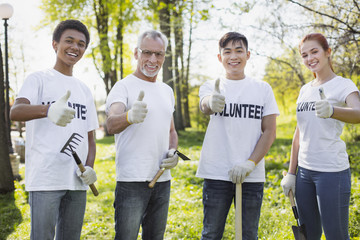 Environmental volunteering option. Merry four volunteers showing thumbs and holding garden tools