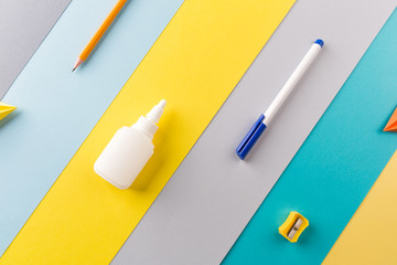 school and office supplies on bright striped background. minimum set in yellow, blue, grey and orange color: pen, pencil, sharpener, glue. concept: back to school, minimalism. Flat lay, top view