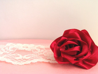 Red rose from a satin ribbon handmade on a pink box, beige braid