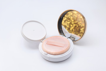 compact case of foundation powder cushion with beige puff and shining golden reflection on white background