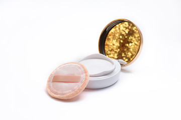 compact case of makeup foundation powder cushion with beige puff and shining golden reflection on white background