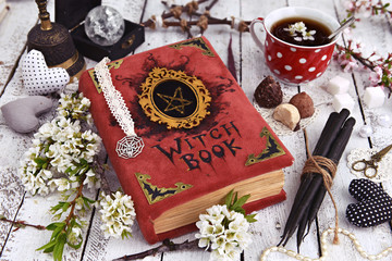 Witch book with black candles, cup of tea and mystic decorations. Occult, esoteric and divination still life. Halloween background with vintage objects 