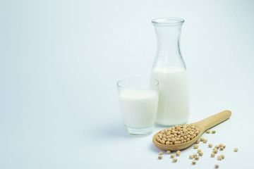 Homemade soy milk in glass bottle with soybeans in wooden spoon on white background