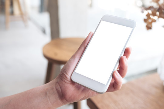 Mockup image of hand holding white mobile phone with blank desktop screen in cafe