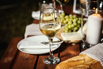 romantic dinner with a glass of wine, a baguette and snacks on an old wooden table on a summer evening