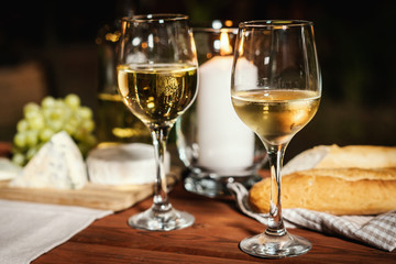 romantic dinner with two glasses of wine, a baguette and snacks on an old wooden table on a summer evening