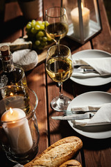romantic dinner with two glasses of wine, a baguette and snacks on an old wooden table on a summer evening