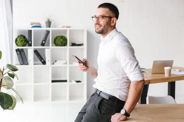 Image of executive director man in formal wear sitting on table in office and looking through big...