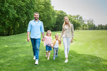 happy family holding hands and smiling at camera while walking together in park