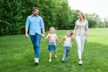 Obraz premium happy family holding hands and walking together in park