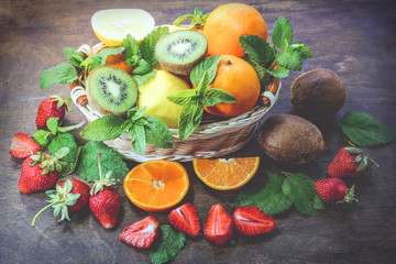 citrus fruits in a basket and strawberries on a wooden background