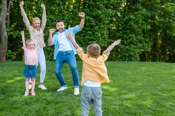 Obraz premium cheerful family raising hands and smiling each other in park