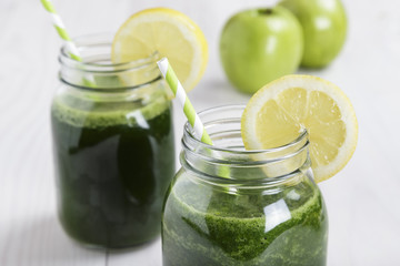 Spinach with lemon and apple juice a soft drink jar with straw on white wooden table