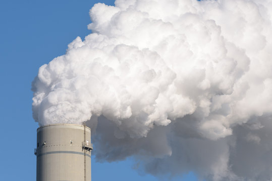 A smokestack of a coal power plant with white smoke against a blue sky