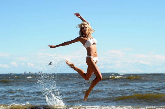 beautiful blonde in a swimsuit is jumping near the sea