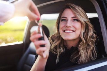 An attractive woman in a car gets the car keys. Rent or purchase of auto.