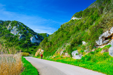 The trail, the pedestrian, car-free zone in the valley of the Alcabrichel River, surrounded by evergreen trees on steep hills. People walking along the road. Landscape near Vimeiro in Portugal.