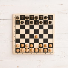 Top view on wooden chess board with figures on white wooden table background. First chess move.