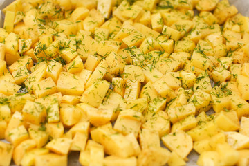 close up cut potatoes with seasoning and dill on a tray in selective focus
