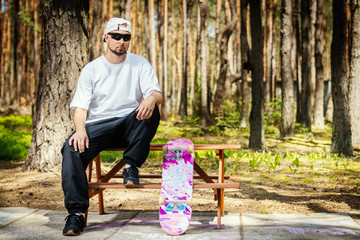 man in a white cap with a skateboard sits on a picnic table in a summer park © superelaks