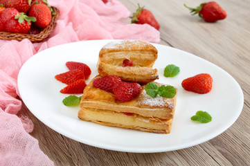 Sweet tasty puff pastry dessert on a plate on a wooden background. Delicious homemade cookies with strawberry jam, berries and sugar powder