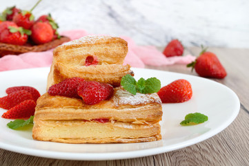 Sweet tasty puff pastry dessert on a plate on a wooden background. Delicious homemade cookies with strawberry jam, berries and sugar powder