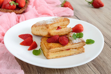 Sweet tasty puff pastry dessert on a plate on a wooden background. Delicious homemade cookies with strawberry jam, berries and sugar powder