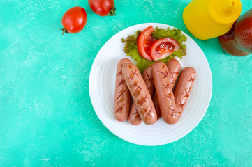 Delicious juicy grilled sausages on a plate, vegetables, ketchup and mustard on a bright background. The top view