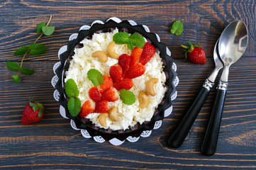 A bowl of fresh home-made cottage cheese with strawberries, mint and nuts on a wooden background. Useful breakfast. Proper nutrition. The top view