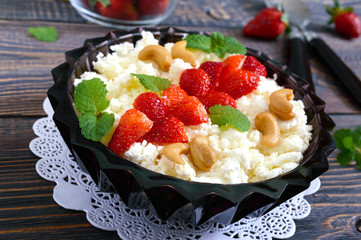 A bowl of fresh home-made cottage cheese with strawberries, mint and nuts on a wooden background. Useful breakfast. Proper nutrition.