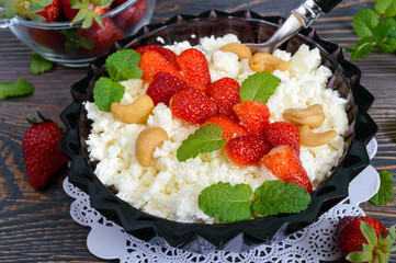 A bowl of fresh home-made cottage cheese with strawberries, mint and nuts on a wooden background. Useful breakfast. Proper nutrition.