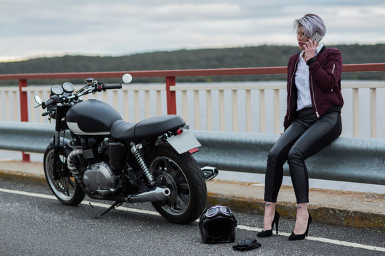 Attractive woman talking with smartphone next to her motorbike