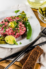 French cuisine, beef steak tartare with raw quail egg yolk, pickled cucumber and onions, fresh herbs, bread, white marble background copy space