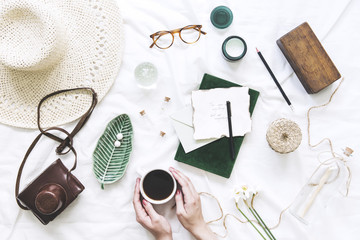 Trendy and stylish flat lay with woman hands on cup of coffee, accessories, hat, glasses, letters and notebook. Lifestyle and blogger concept.