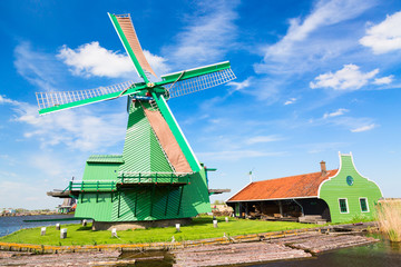 Dutch typical landscape. Traditional old dutch windmill against blue cloudy sky in the Zaanse Schans village, Netherlands. Famous tourism place.
