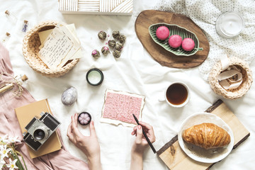 Trendy flat lay of workspace with woman hands on pink card,  accessories, cakes and retro photo camera. Lifestyle and influencer blogg concept. Copy space. 
