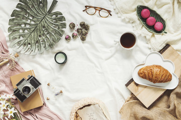 Flat lay of workspace in bed with notebook, camera, cup of coffee, woman accessories on white...