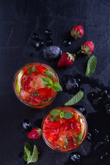 Strawberry mojito cocktail with berries, lime, mint and ice, black background. Summer berry cocktail. View from above, top studio shot