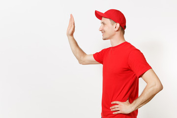 Delivery man in red uniform isolated on white background. Male in cap, t-shirt working as courier or dealer, waving and greeting with hand as notices someone. Copy space for advertisement. Side view.