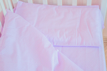 Baby bedding and quilted blanket in a white crib of tender lilac color