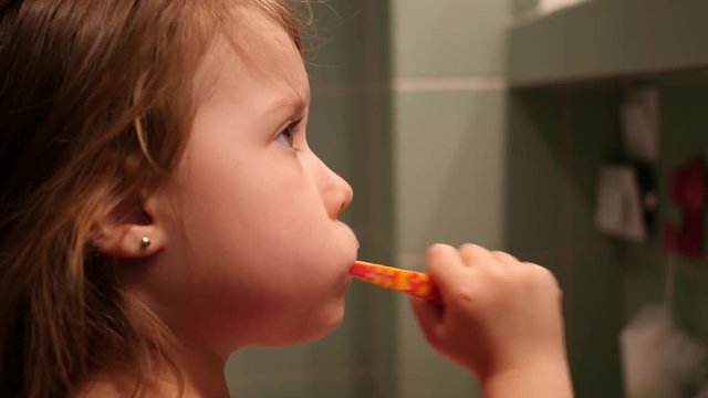 Little child girl face portrait brushing her teeth with a toothbrush in bathroom in the morning