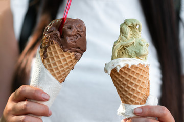 Female hands are holding two melting gelato. chocolate and pistachio flavor in the cones. close-up view