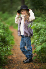 Spring portrait of a little girl.Sweet girl with big brown eyes in a black hat and a fur vest. In the background tree.